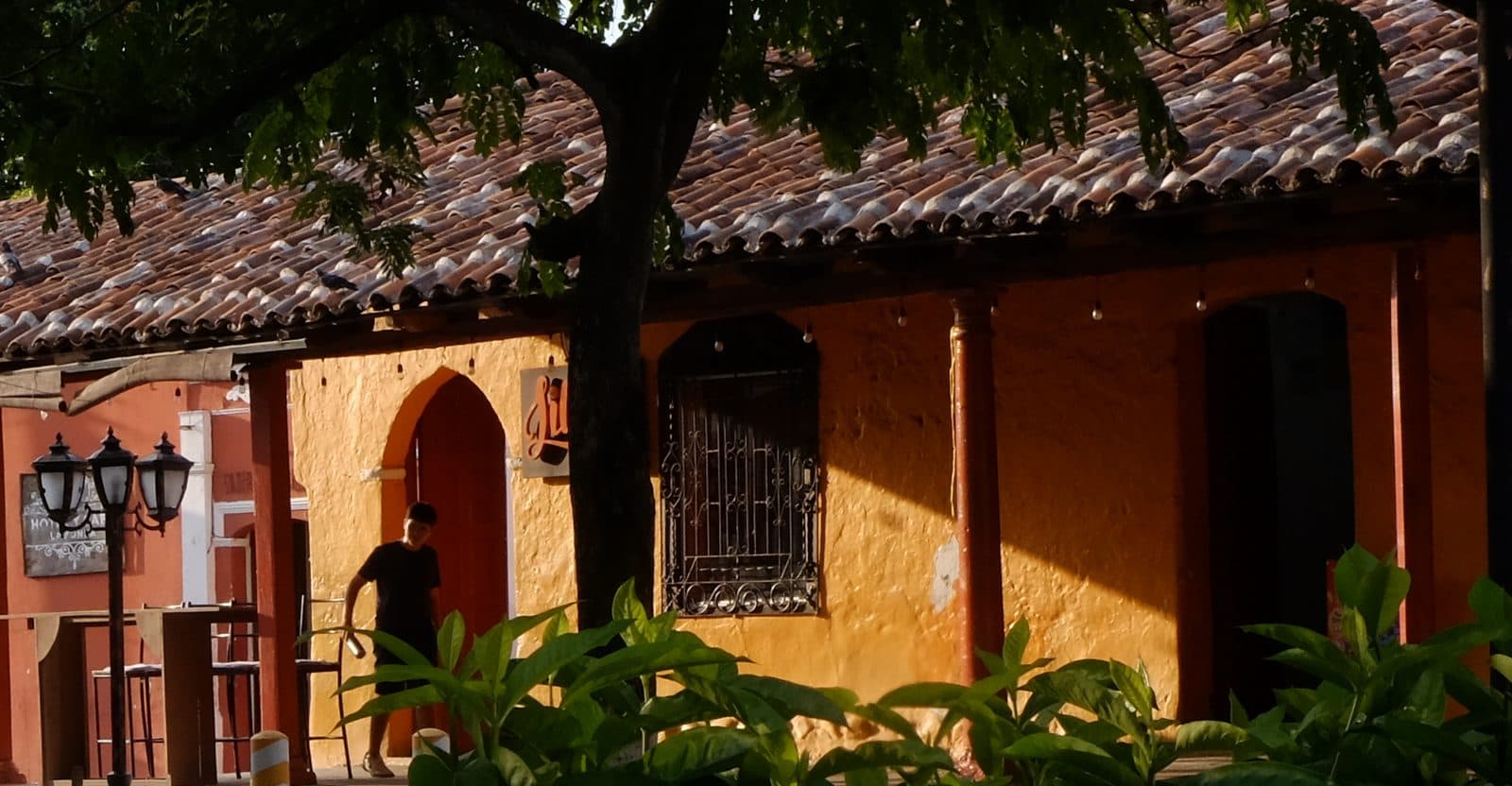 Clay-tiled colonial façade with an arched doorway and a wrought-iron window on the Suchitoto plaza