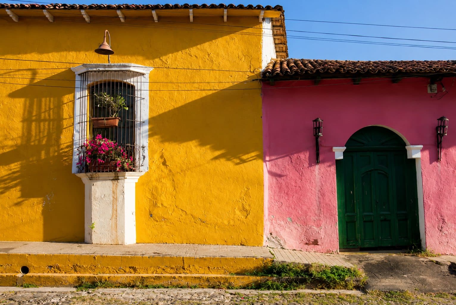 Ochre and rose façades with a grilled timber window and a green wooden door